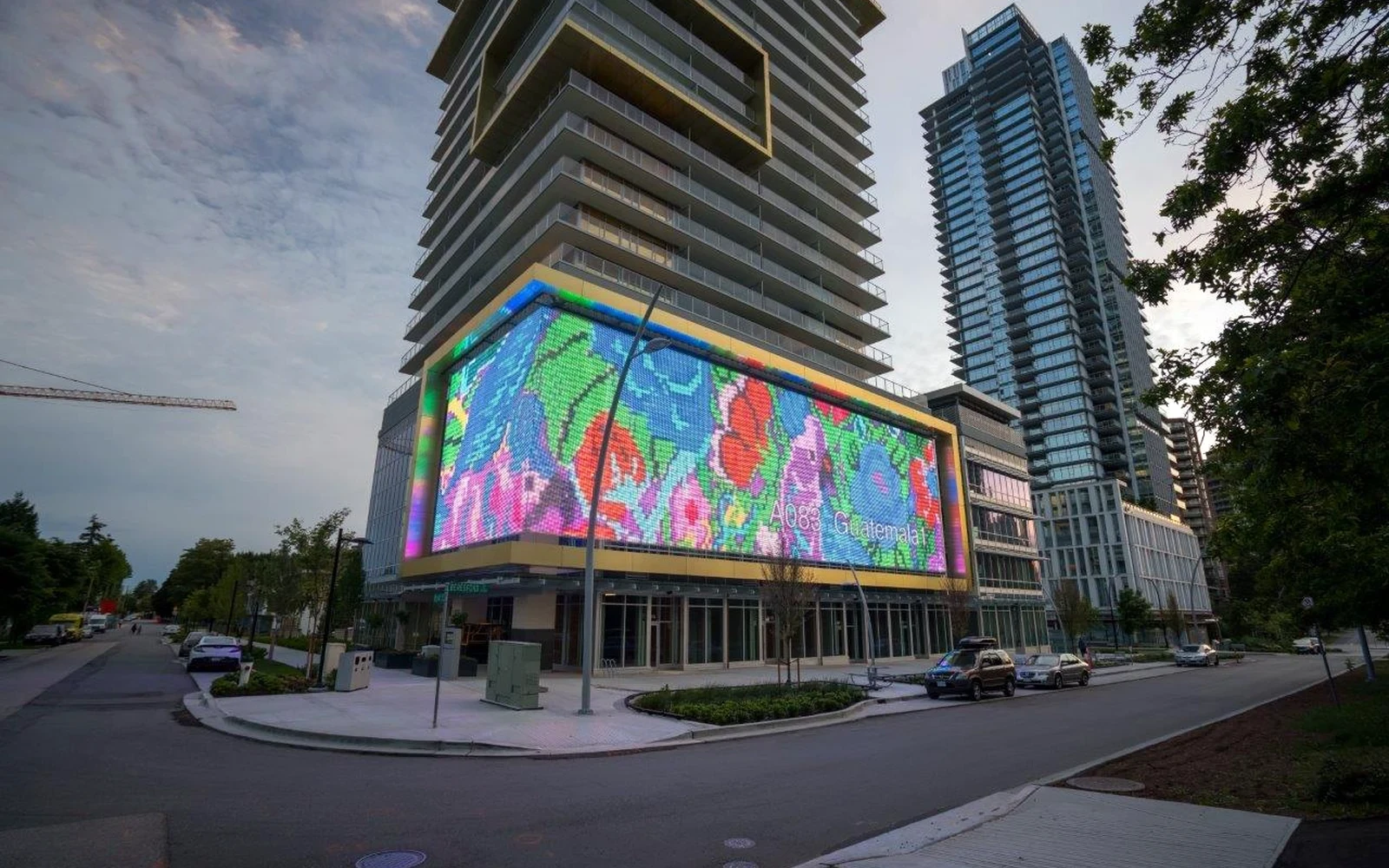 Outdoor LED screen wrapped around the base of a residential tower at dusk